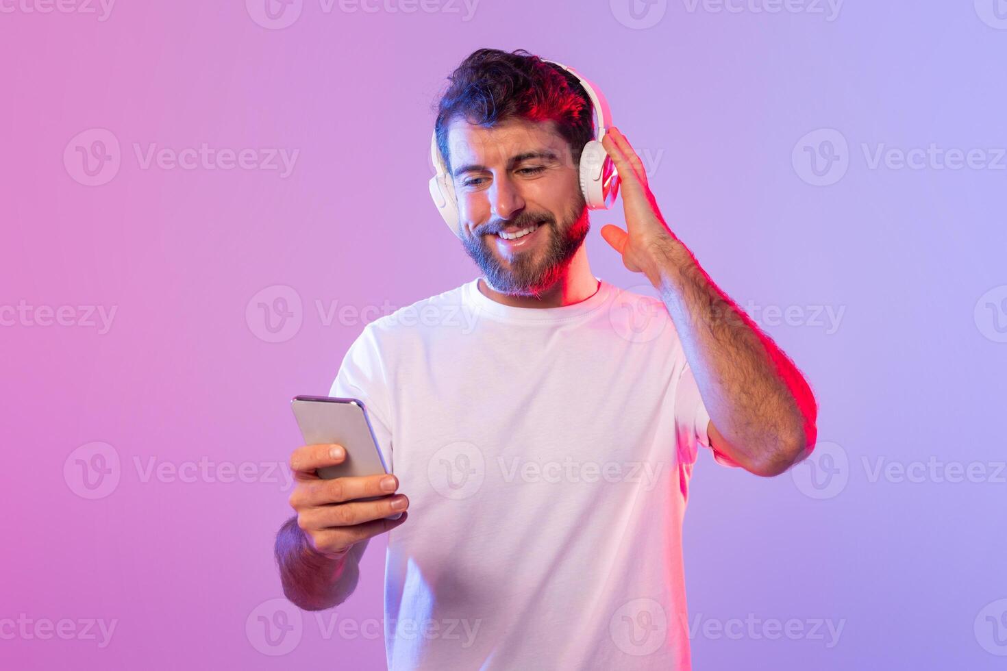 A man is sitting and listening to music through headphones while holding a cell phone in his hand. He appears focused on the music playing and the content on his phone screen. photo