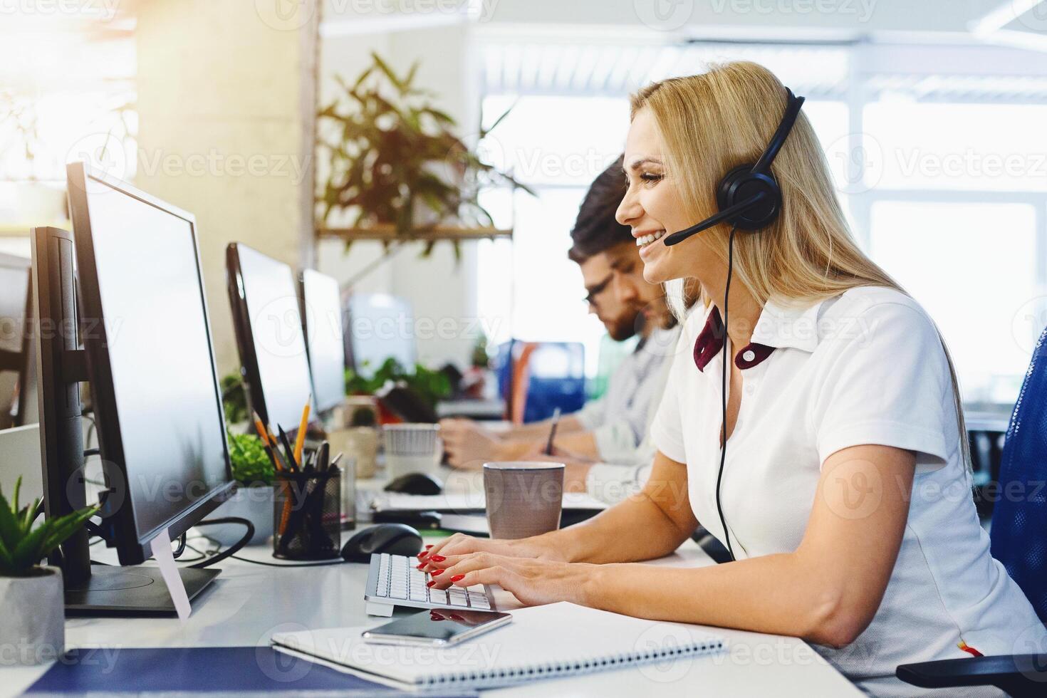 Smiling young woman in headset working in open-space office, call center of big company, empty space photo