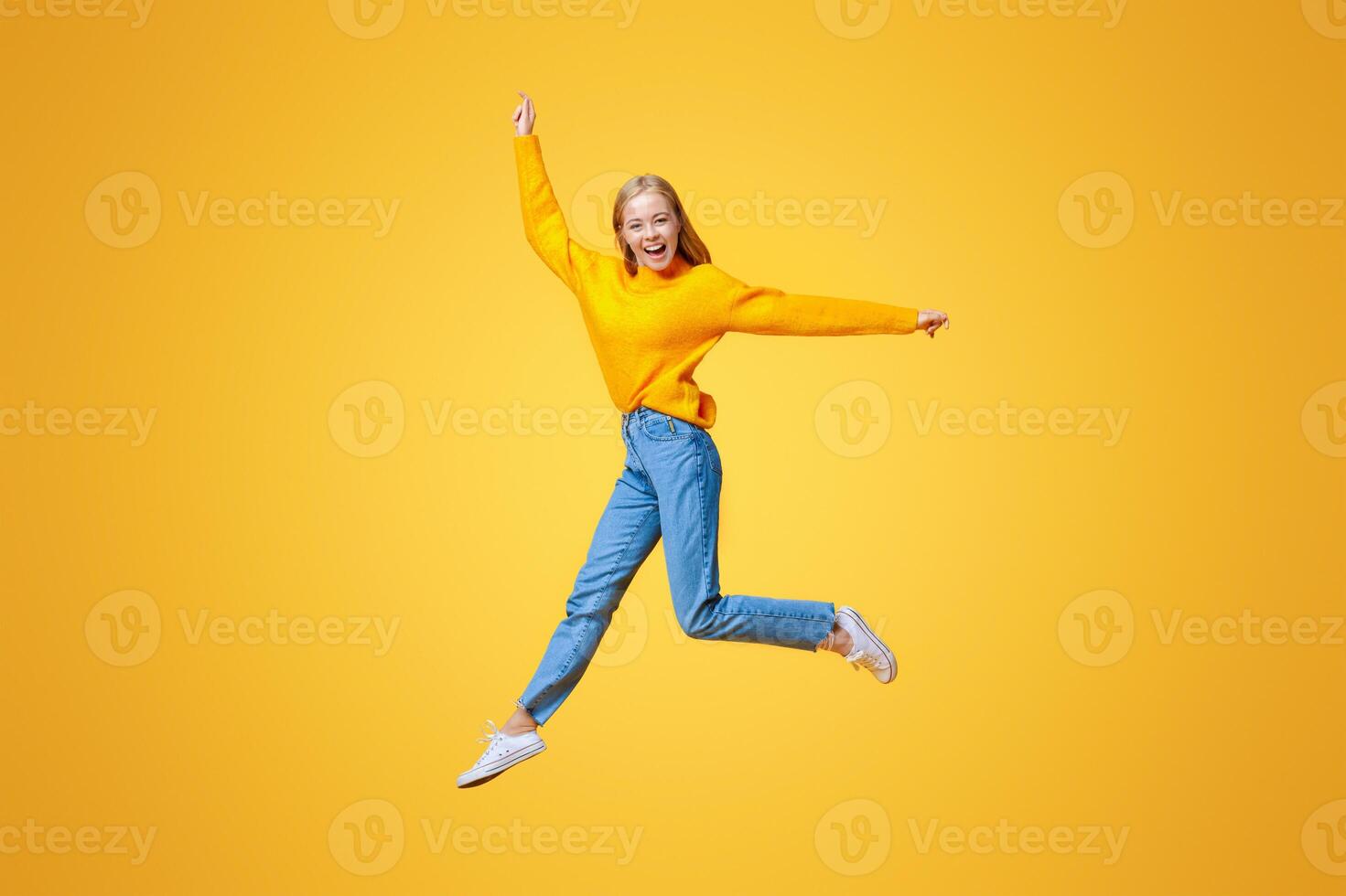 Jumping millennial girl in the air over orange studio background with free space photo