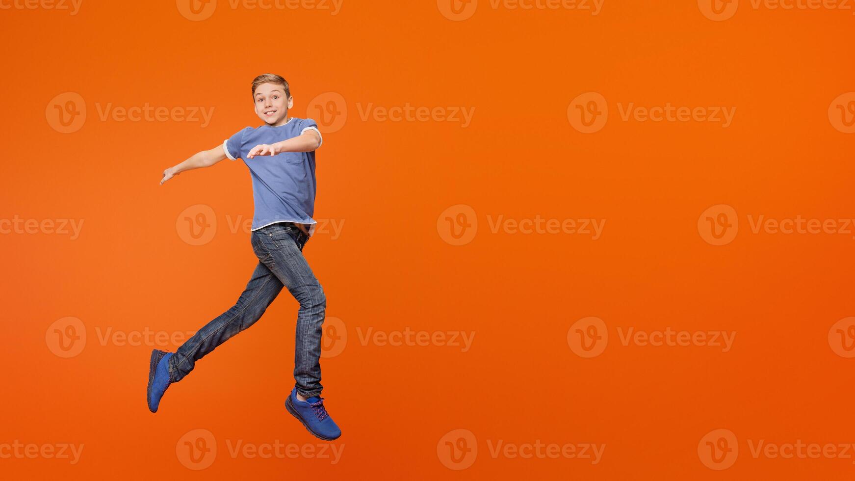 Cute carefree boy dancing, jumping in air, having fun on orange background photo