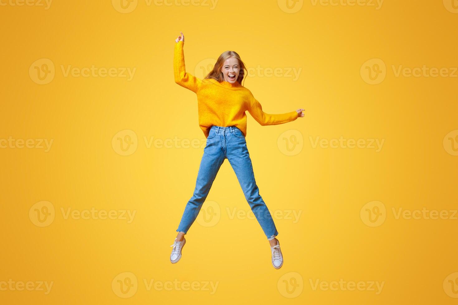 Euphoric teen girl jumping in air with hands up, orange studio background with empty space photo