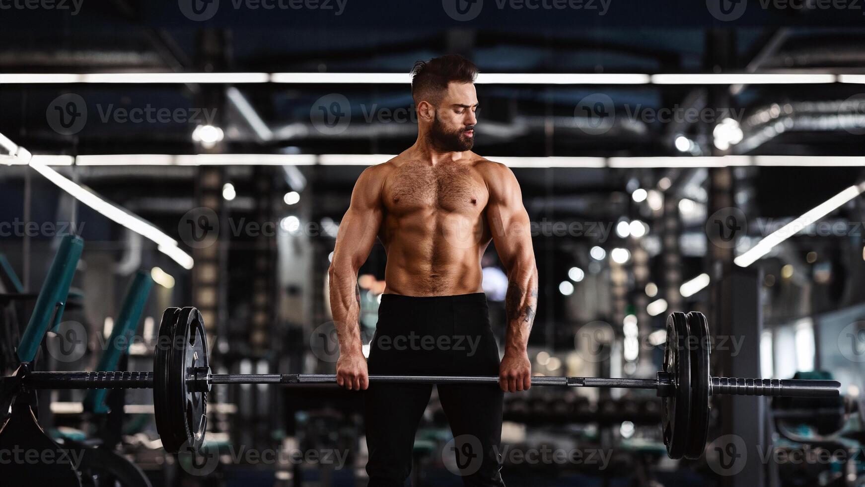 Muscular athletic bodybuilder training arms with barbell in gym, working out with naked torso, free space photo