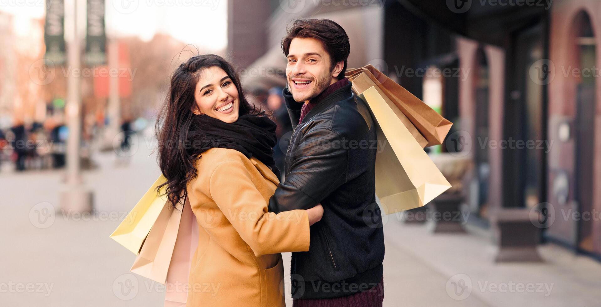 A man and woman walk down a bustling city street, each carrying multiple shopping bags filled with purchases. photo