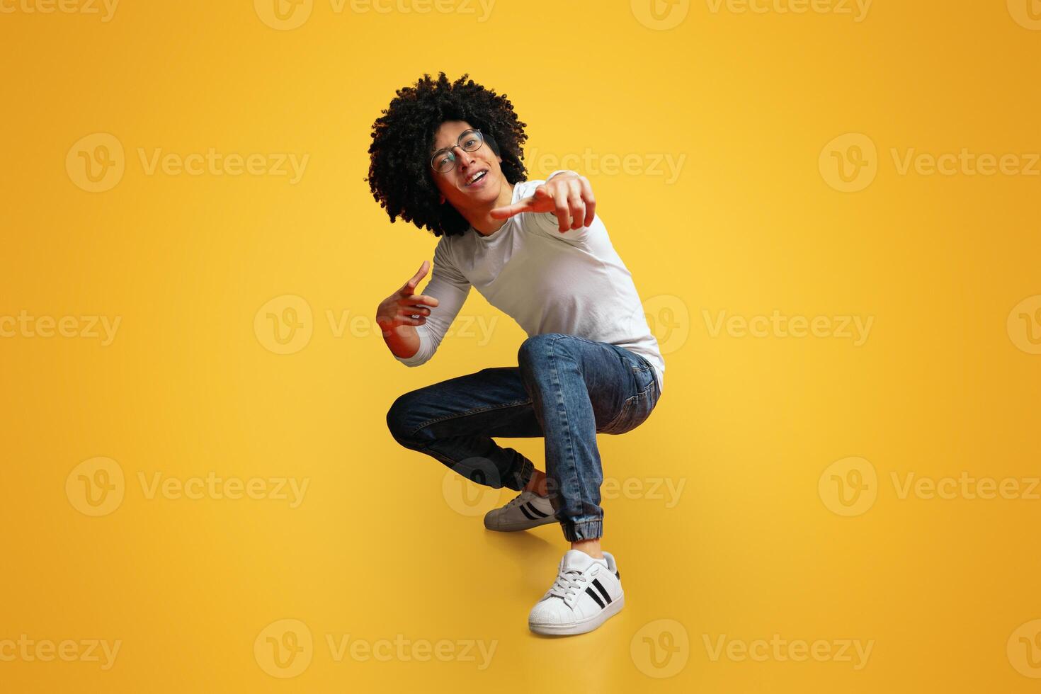 Hey you. Cocky millennial guy pointing at camera, making challenge, squatting on orange studio background photo