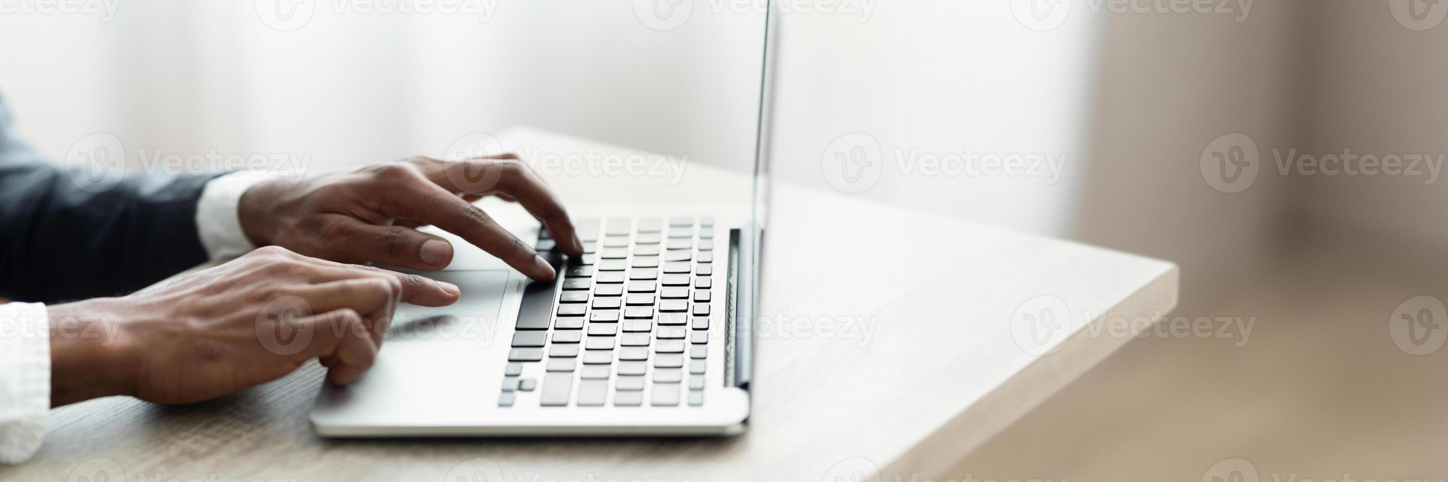 Cropped of african american man in suit typing on laptop keyboard, entrepreneur sending emails, office interior, panorama with copy space photo