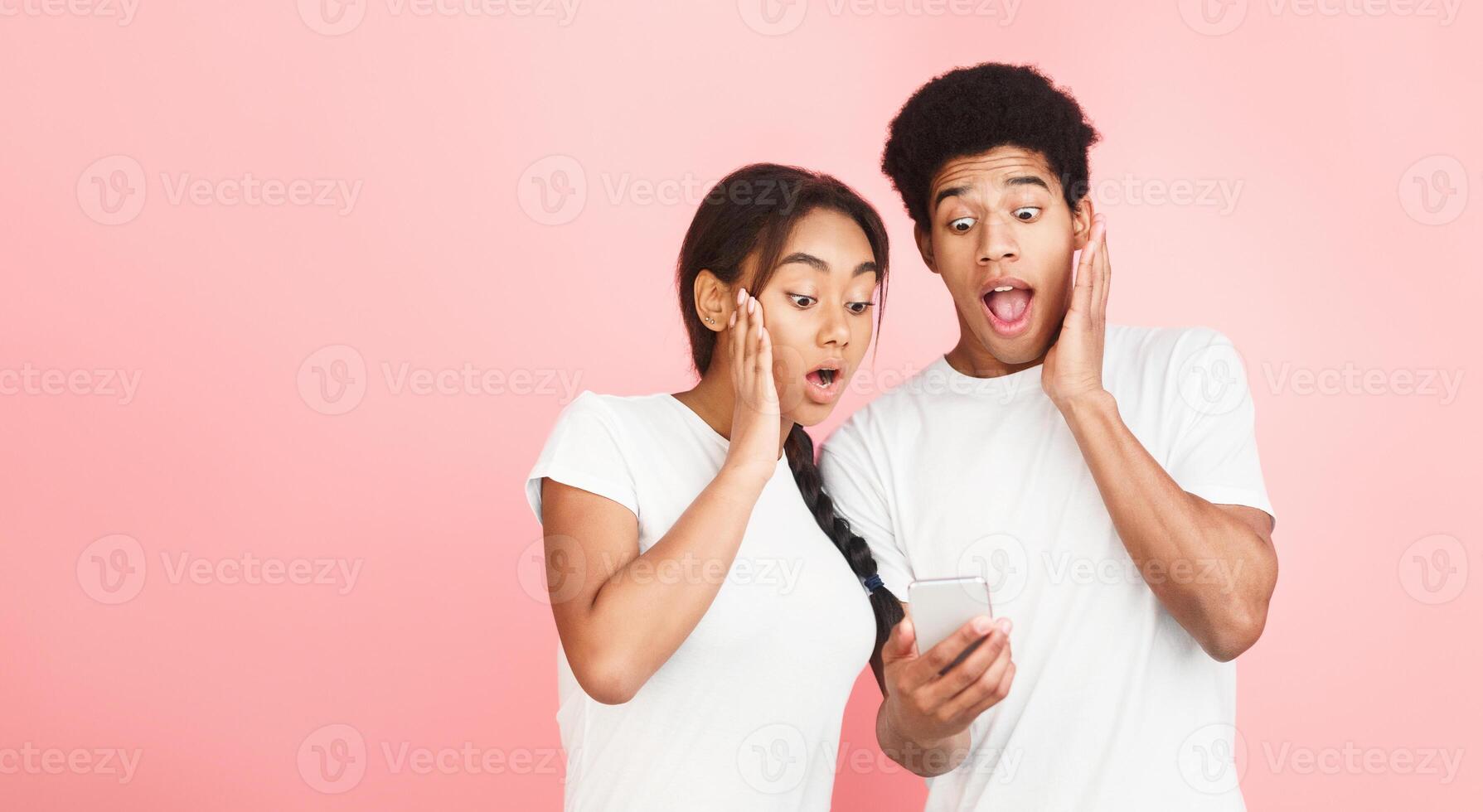 Shock content. Couple using smartphone with surprised expressions over pink background photo
