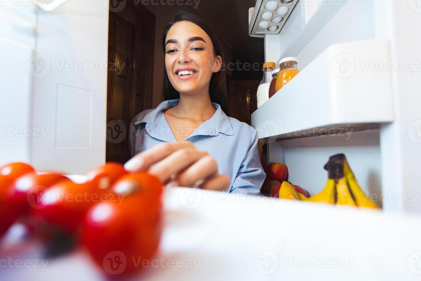 Preparing healthy lunch. Young woman taking fresh tomato from refrigerator, view from inside, empty space photo