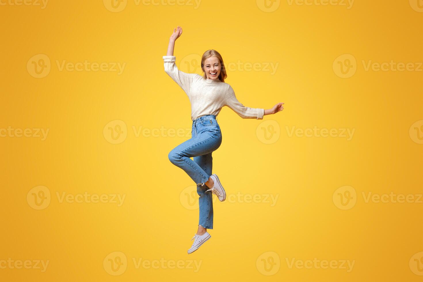 Happy teen girl having fun, jumping on orange studio background with copy space photo
