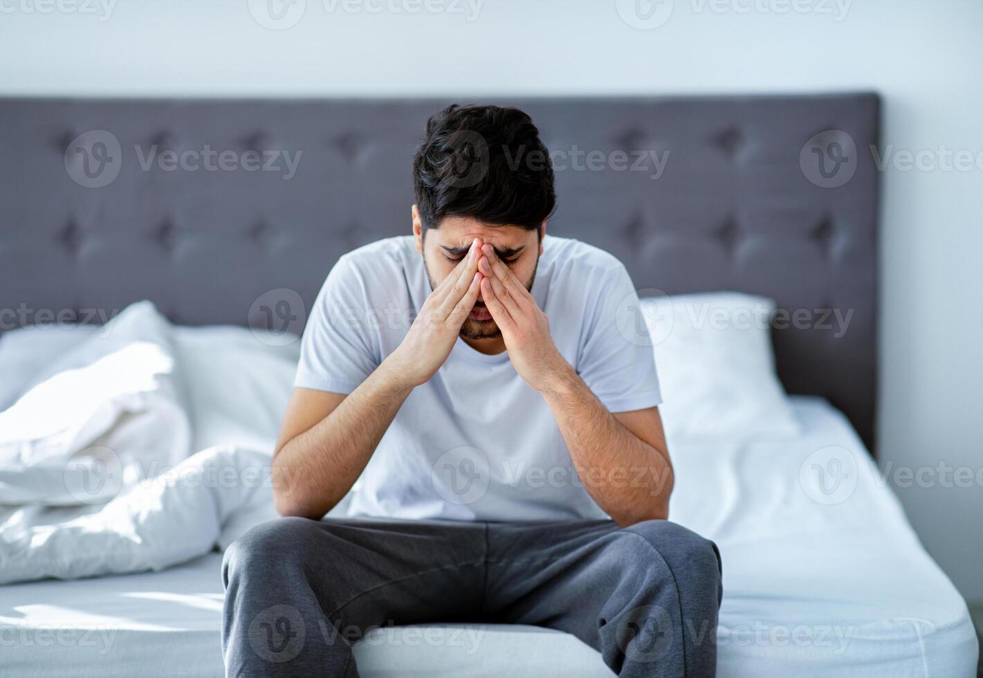 Male depression. Unhappy arab man sitting on bed and thinking about problems, closing face with hands, copy space. Stress, apathy and mental health issue concept. photo
