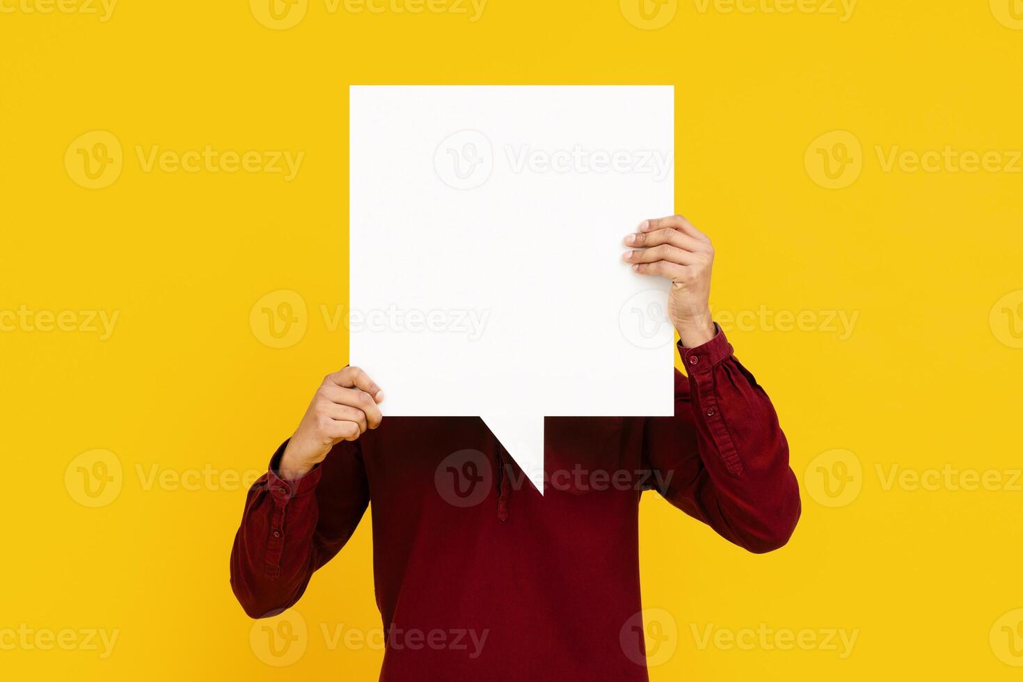 Man is shown holding a white speech bubble in front of his face. The speech bubble is blank, ready to be filled with text. The guy expression is not visible, hidden behind the speech bubble. photo