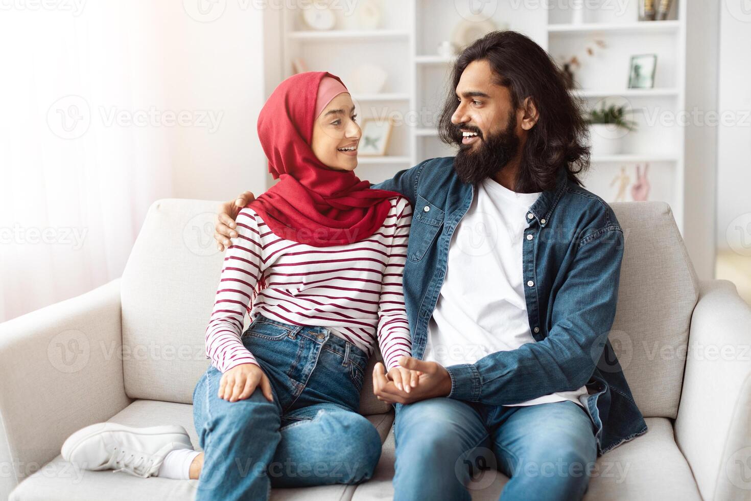 Loving eastern man and a woman are seated together on a couch in a room. They appear to be engaged in conversation or watching television photo