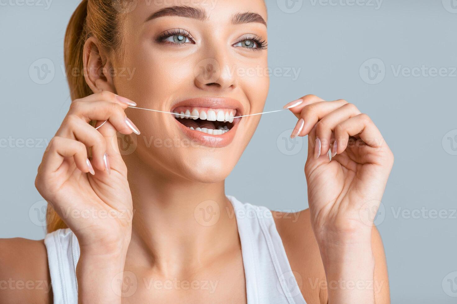 This image shows a woman flossing her teeth with a bright smile. Her bright white teeth and healthy smile are a great example of the importance of proper dental hygiene. photo