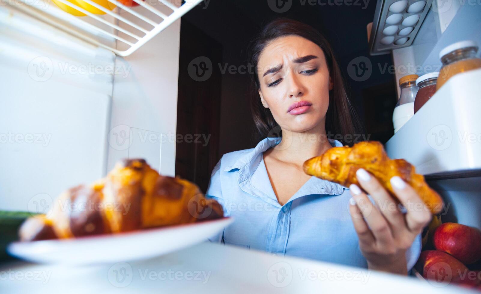 To eat or not to eat. Thoughtful girl looking at croissant with doubt, view from inside of fridge photo