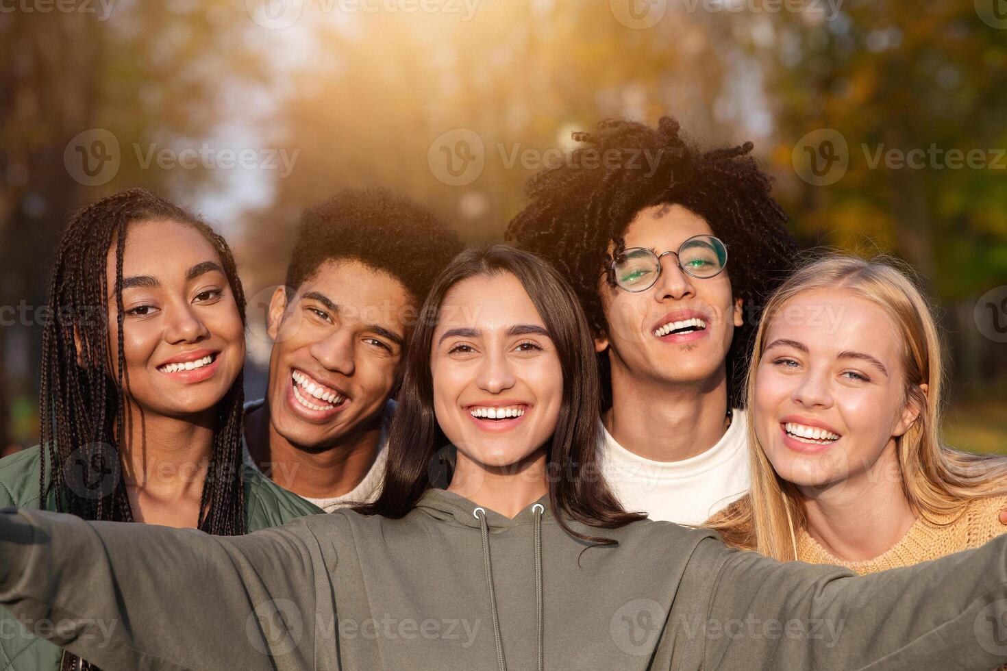 Smiling teen international friends taking selfie while walking in autumn park, happy memories concept photo