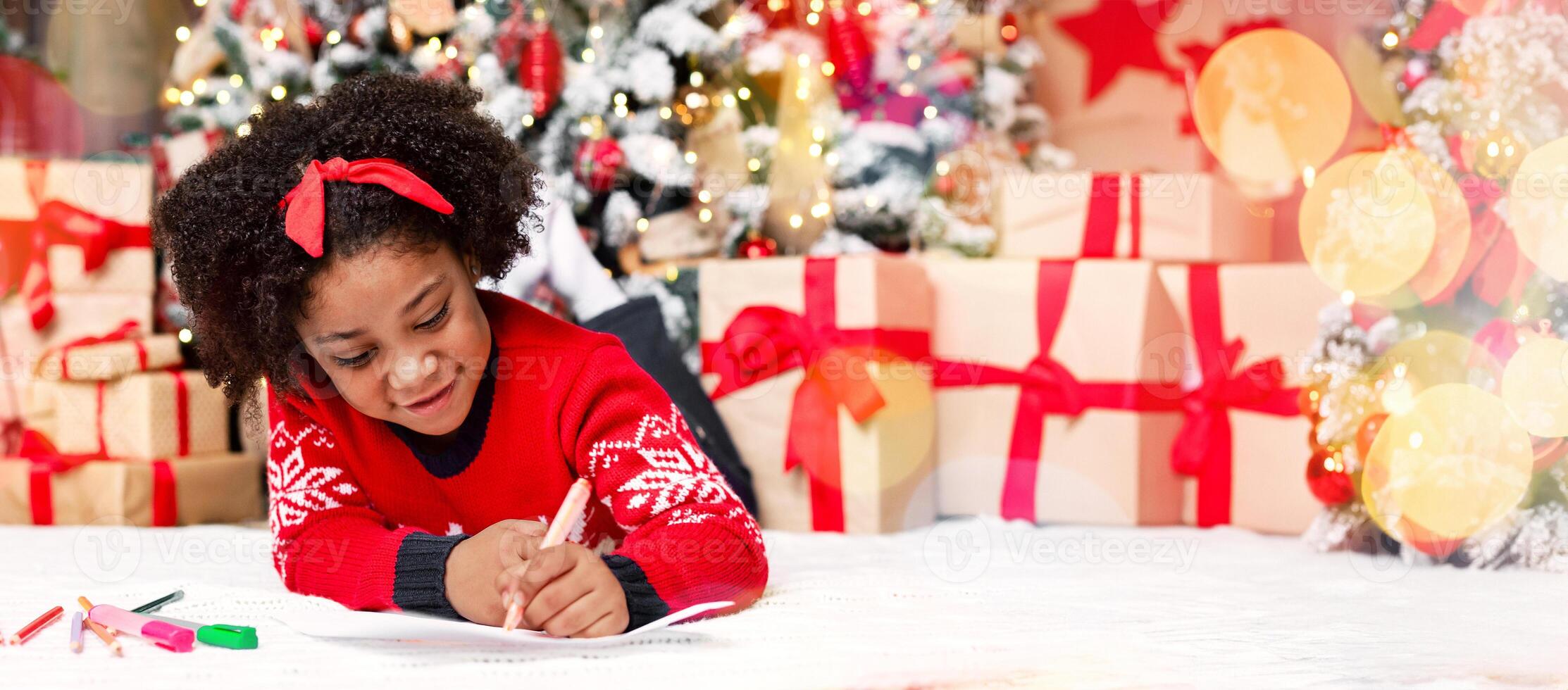 Letter to Santa. Cute little black girl lying on floor and writing wish list of presents for Christmas in decorated room photo