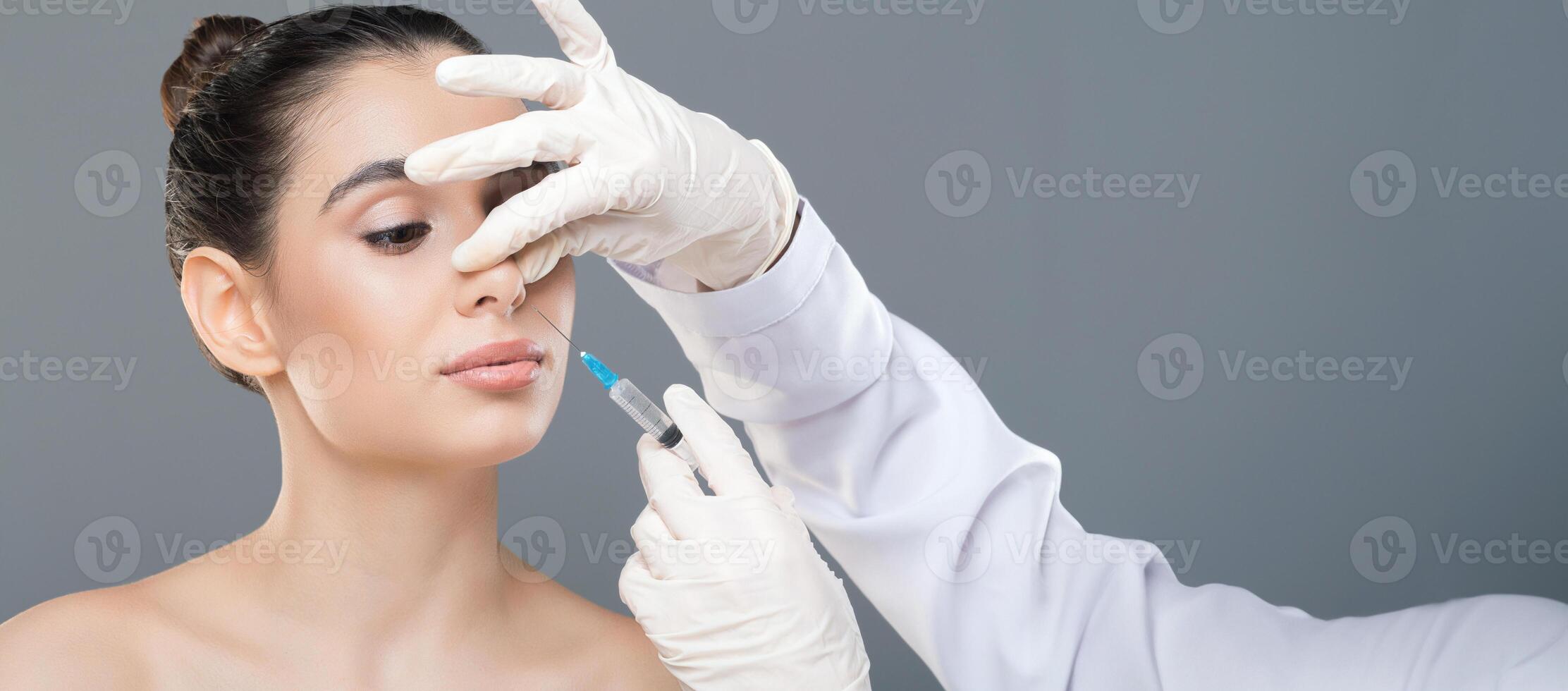 A woman is seated and receiving a cosmetic injection to her nose from a doctor wearing white gloves in a clinical environment. The procedure appears to be focused and meticulous, copy space photo