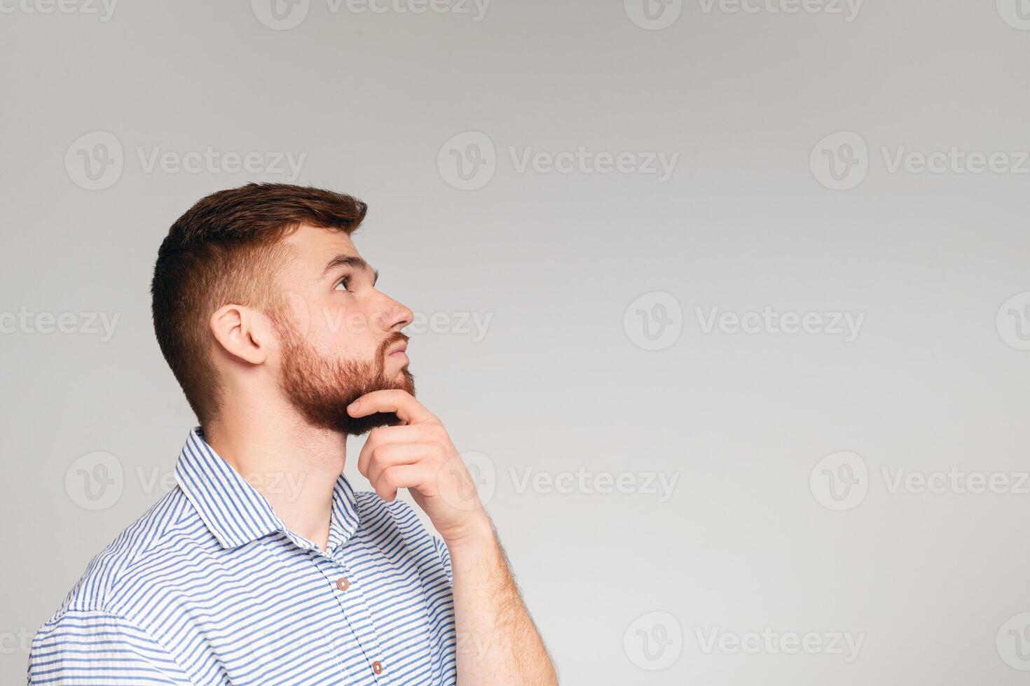 Portrait of thoughtful guy posing isolated on beige studio background, touching his chin, panorama, copy space photo