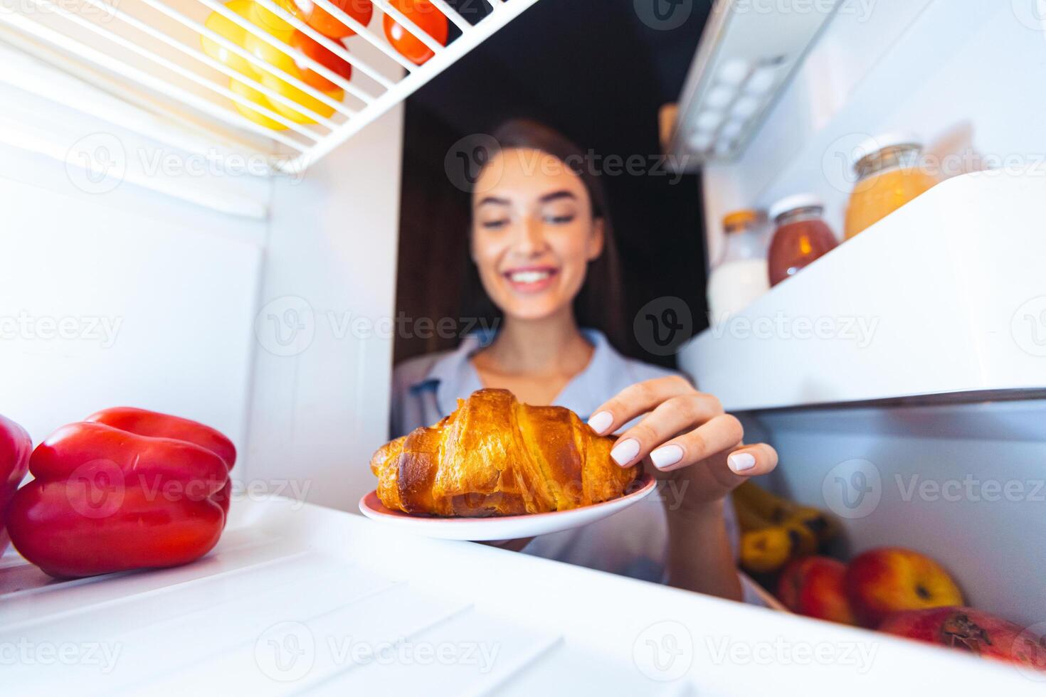 Tasty dessert. Cheerful girl taking yummy croissant from refrigerator at home, view from inside photo