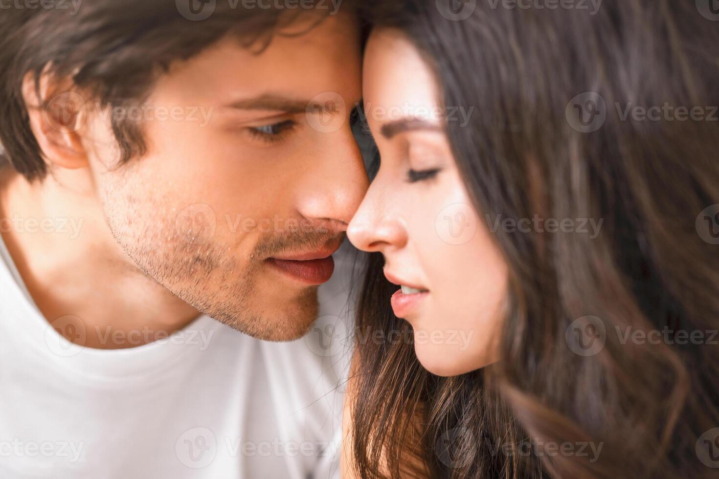 This is a close-up portrait of a man and a woman about to kiss. They are looking into each others eyes and appear to be in love. photo