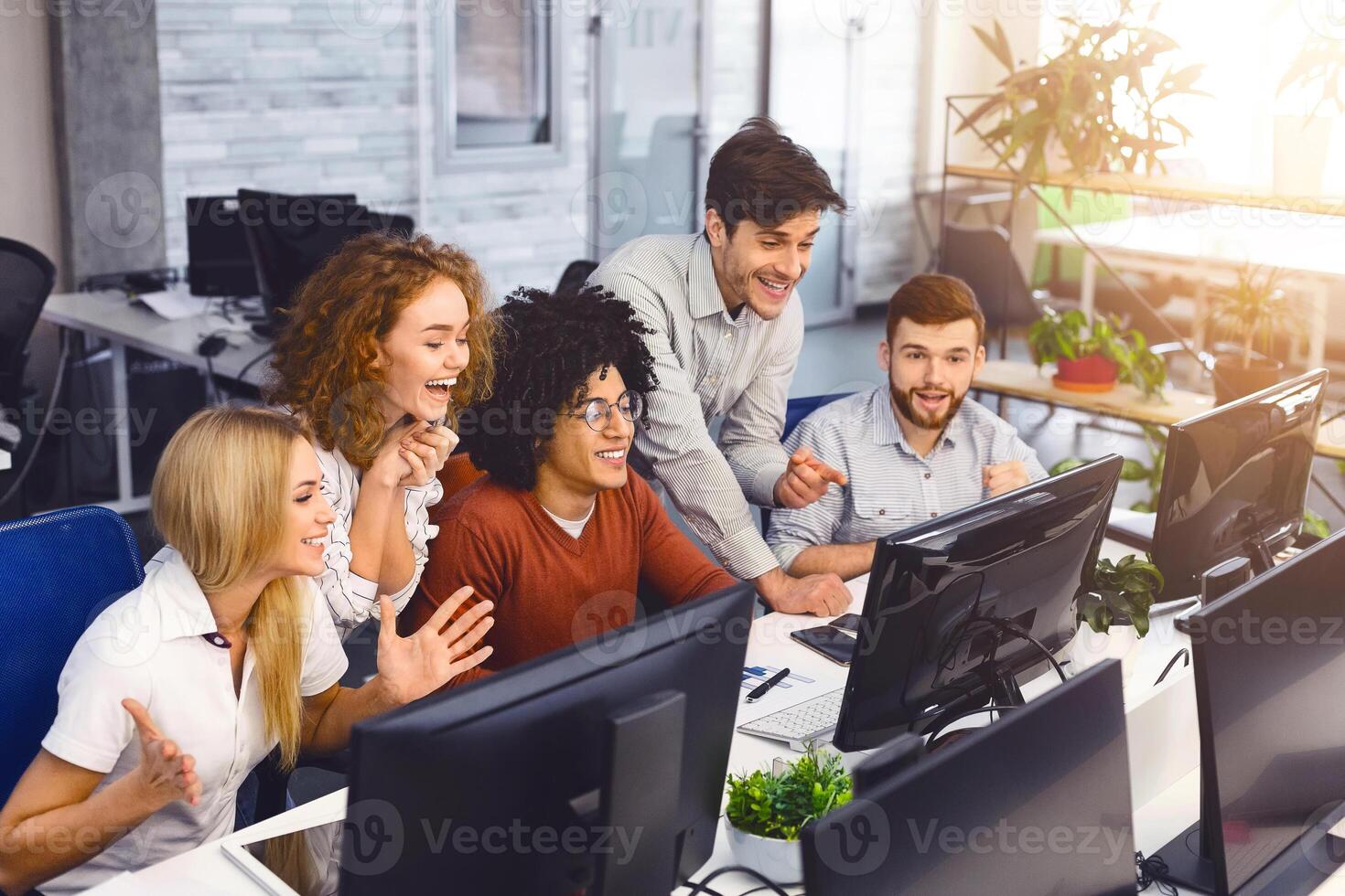 Win grant. Excited students reading good news together on computer screen in modern coworking office, enjoying their friend's success, free space photo