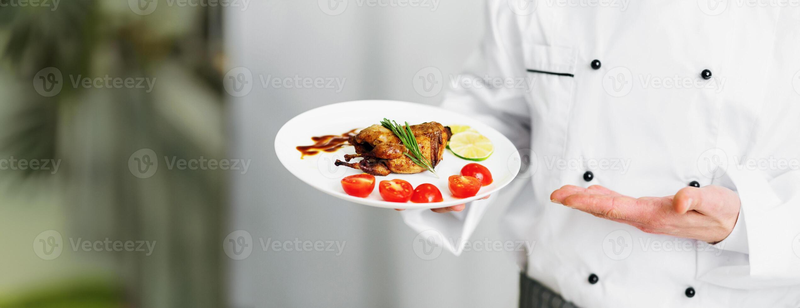 Unrecognizable Chef Guy Holding Plate With Roasted Chicken Presenting Dinner Standing In Kitchen. Cropped, Panorama, Selective Focus photo
