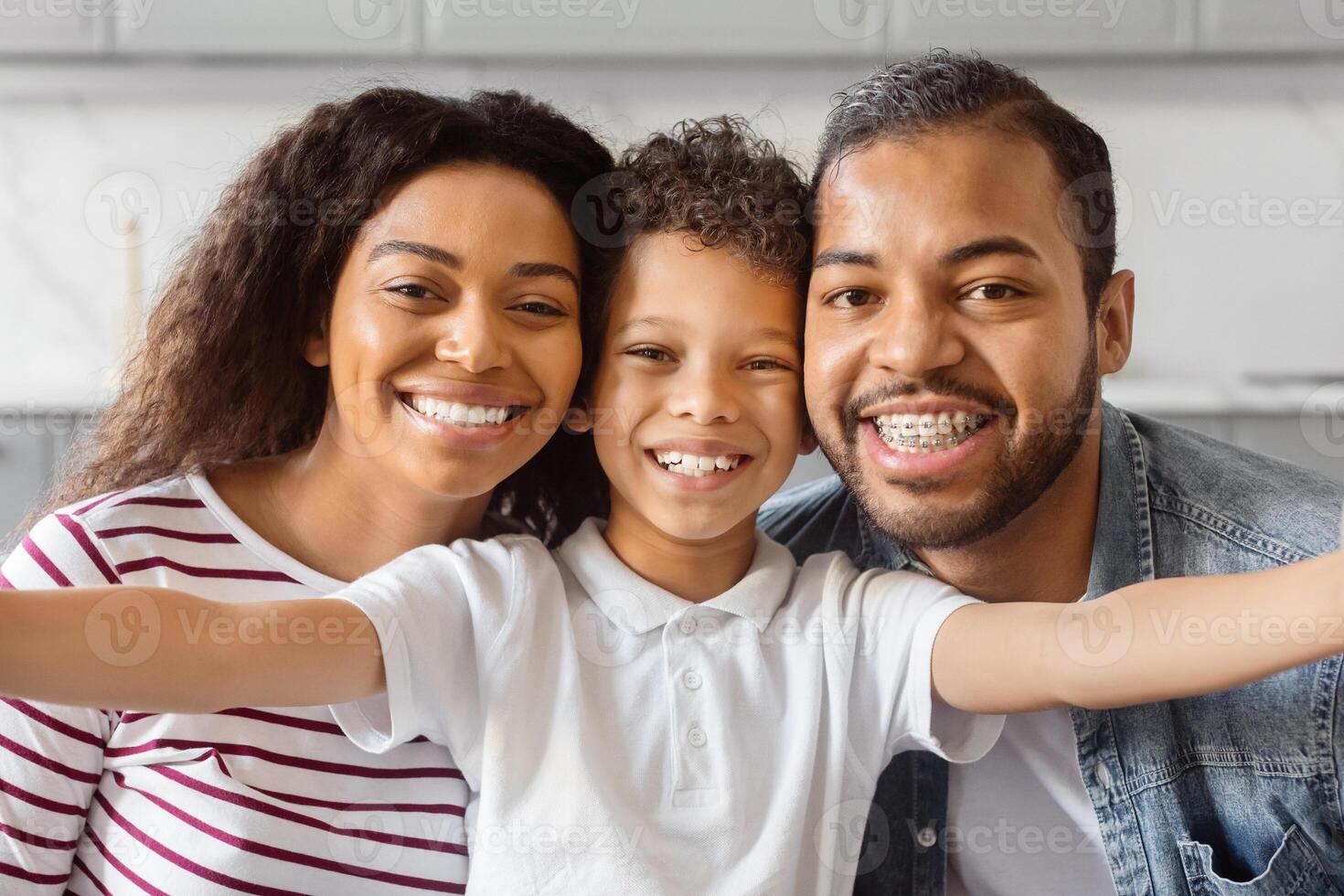 African American man, woman, and child are smiling and posing together while taking a selfie. They are holding a smartphone at arms length and capturing a candid moment of joy and togetherness. photo