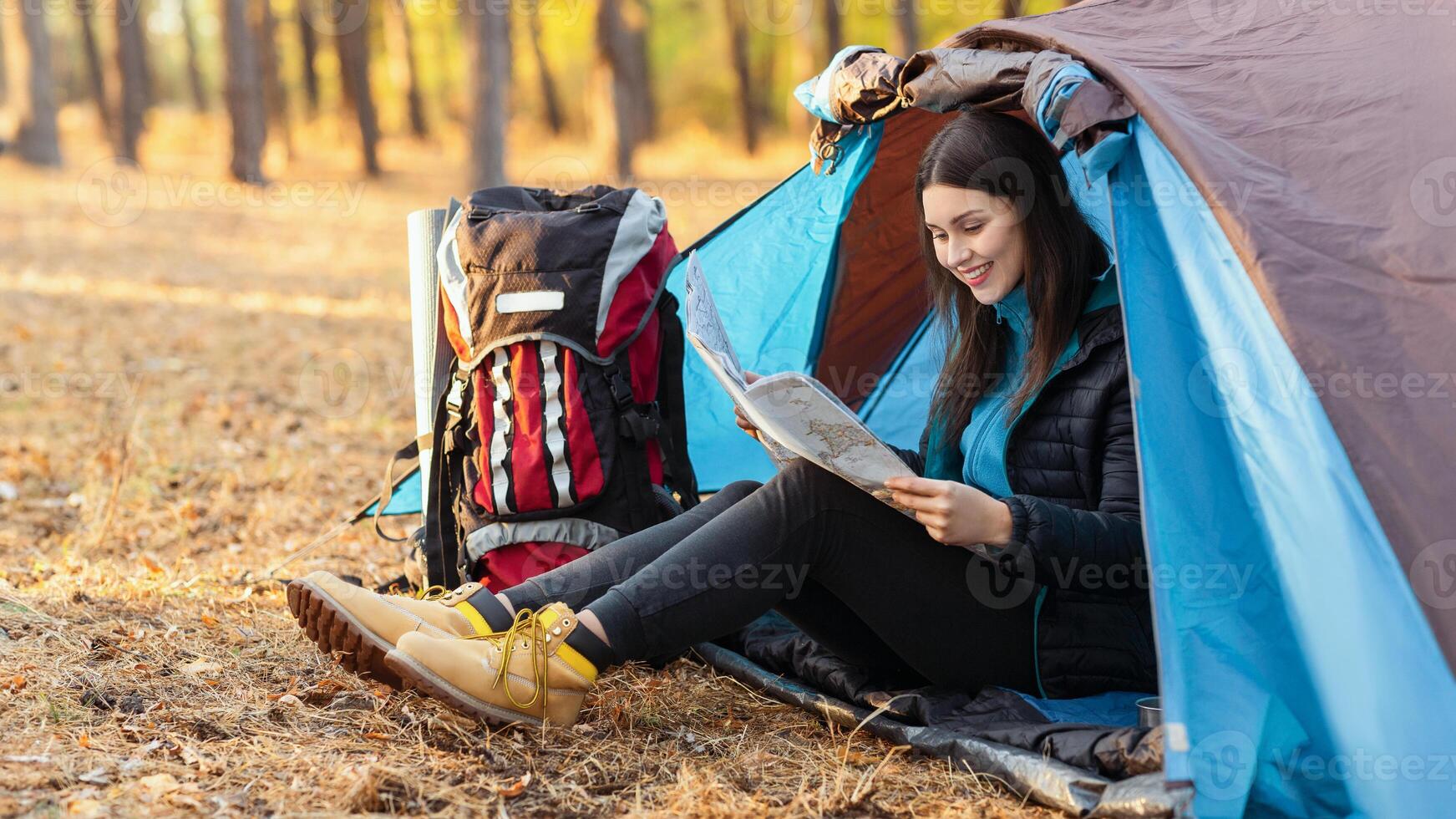 Cheerful girl sitting in tent alone and looking at map, copy space photo
