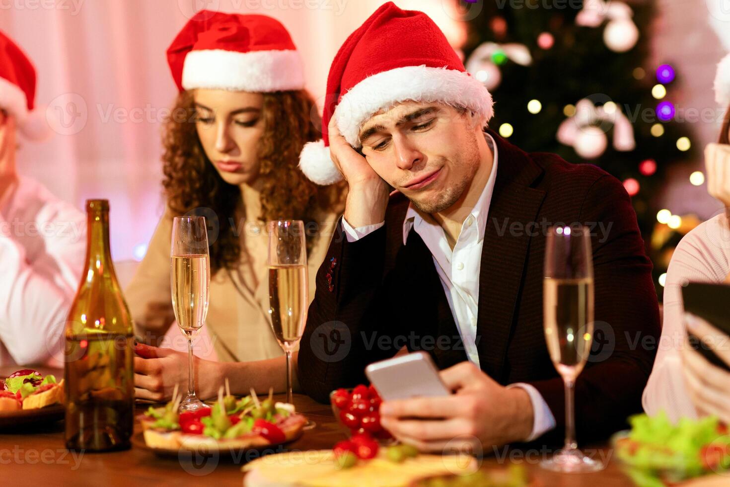 Bad Christmas Party. Bored Guy Using Smartphone During Dreadful Xmas Celebration With Friends At Home. Selective Focus photo