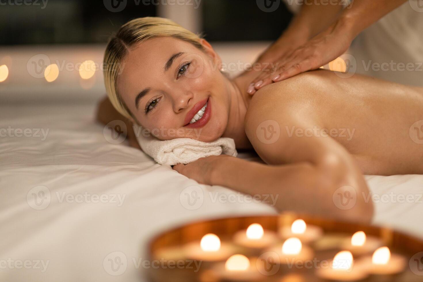 A woman lying face down on a massage table while a professional masseuse is providing a shoulder massage at a luxurious spa. The woman appears relaxed and comfortable photo