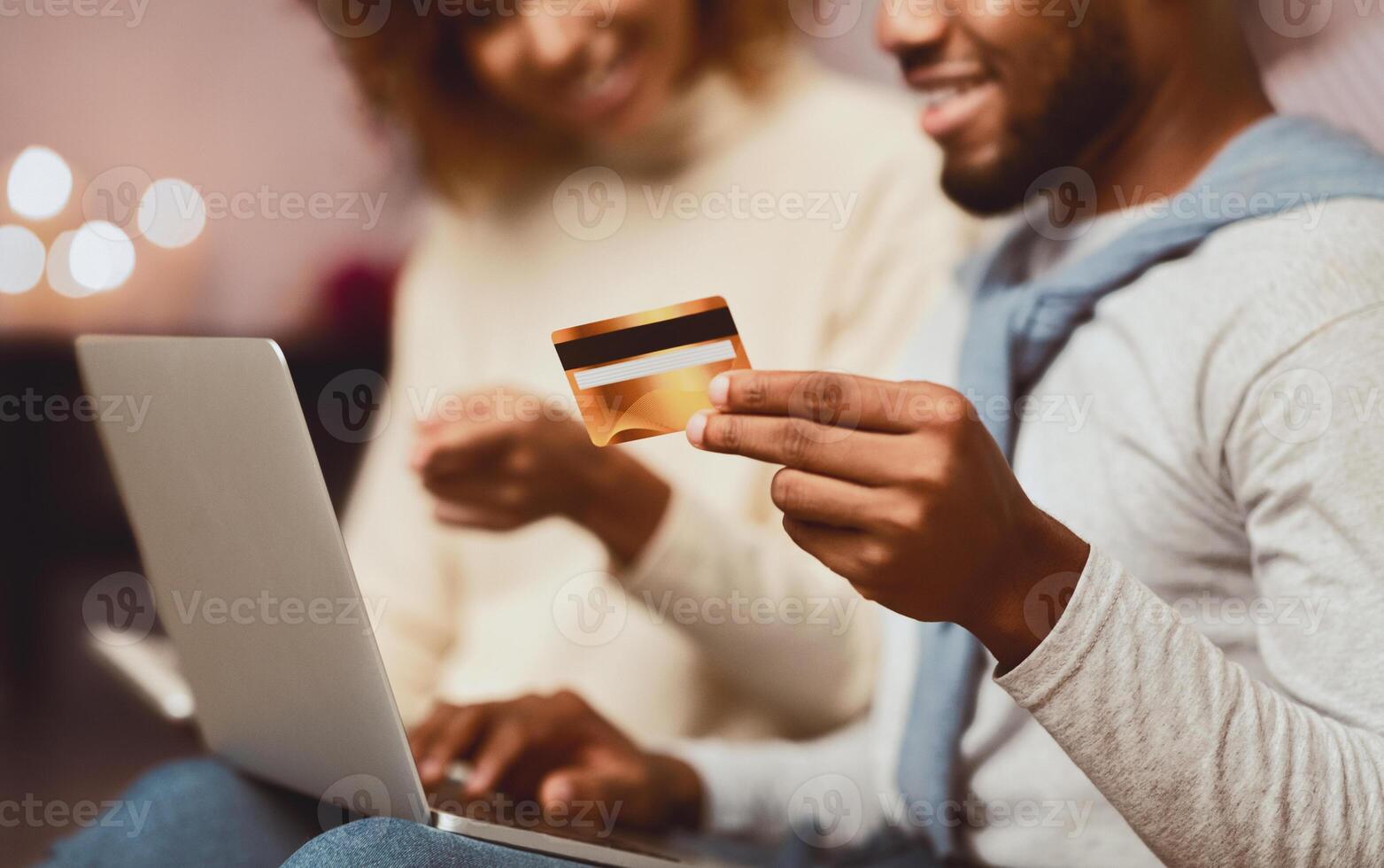 Excited spouses shopping online on laptop, buying Christmas gifts for relatives, focus on credit card photo