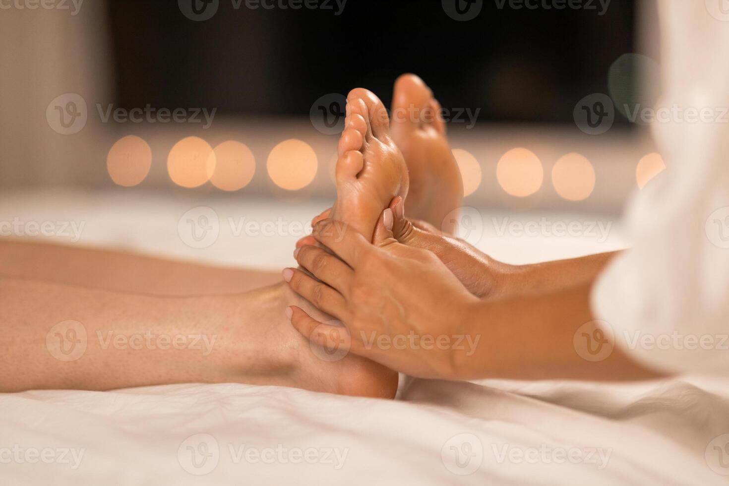 A therapist is performing a relaxing foot massage on a client who is lying down, set against a backdrop of soft, warm ambient lighting that suggests an evening atmosphere designed for relaxation photo
