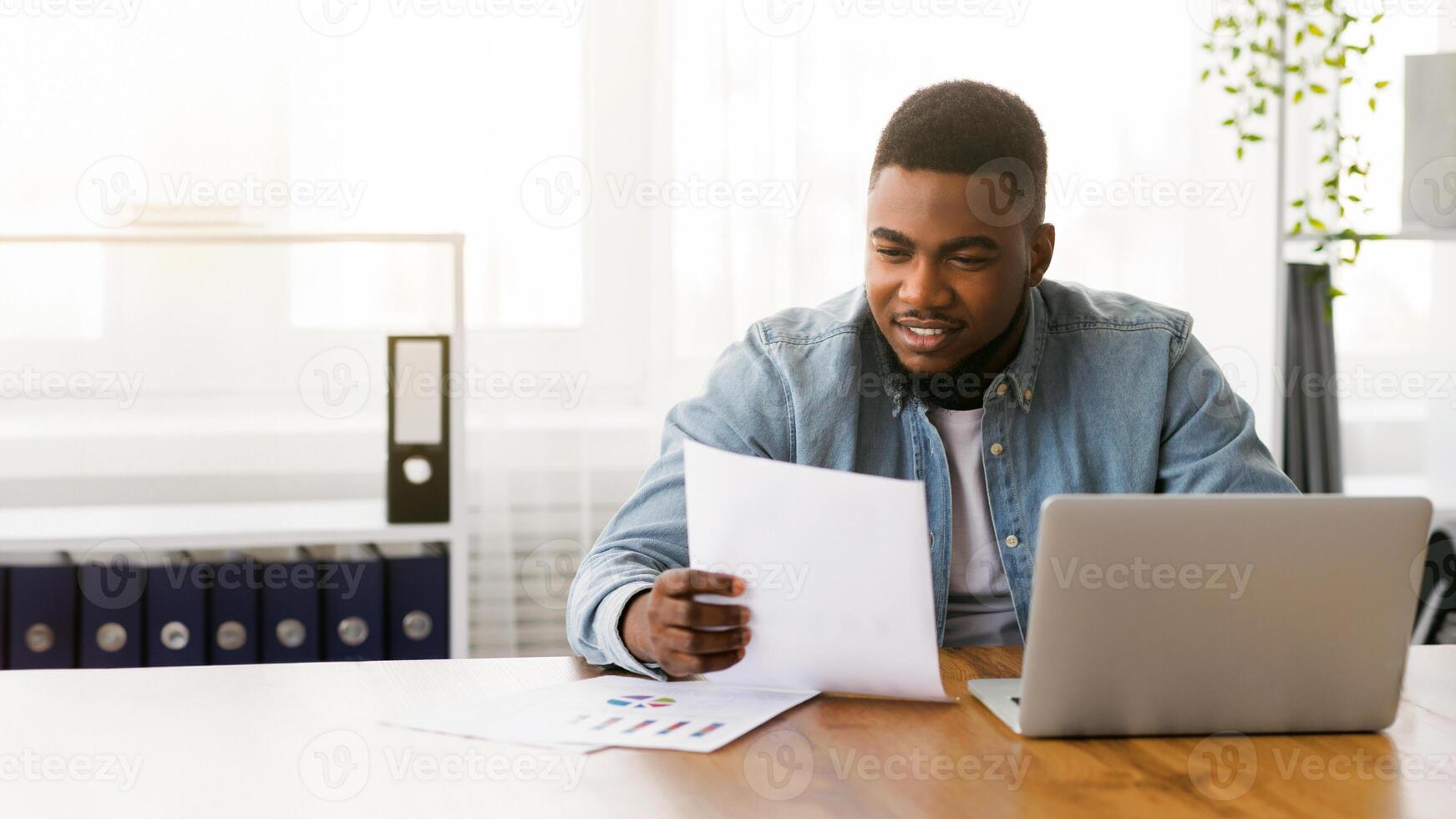 Smiling african american businessman working with documents in office, checking financial reports. photo