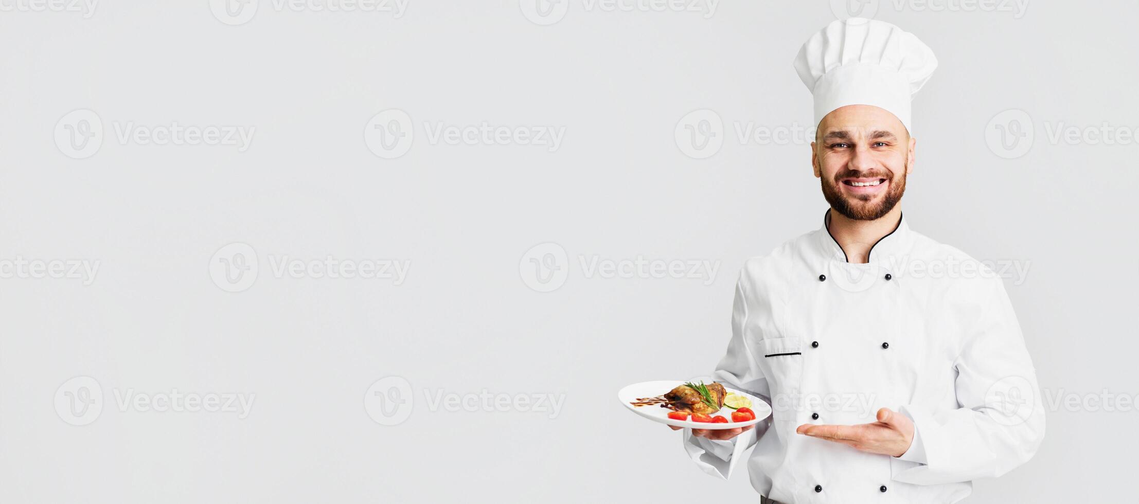 Smiling Male Chef Serving Chicken Dish Holding Plate Standing On Gray Background. Selective Focus photo