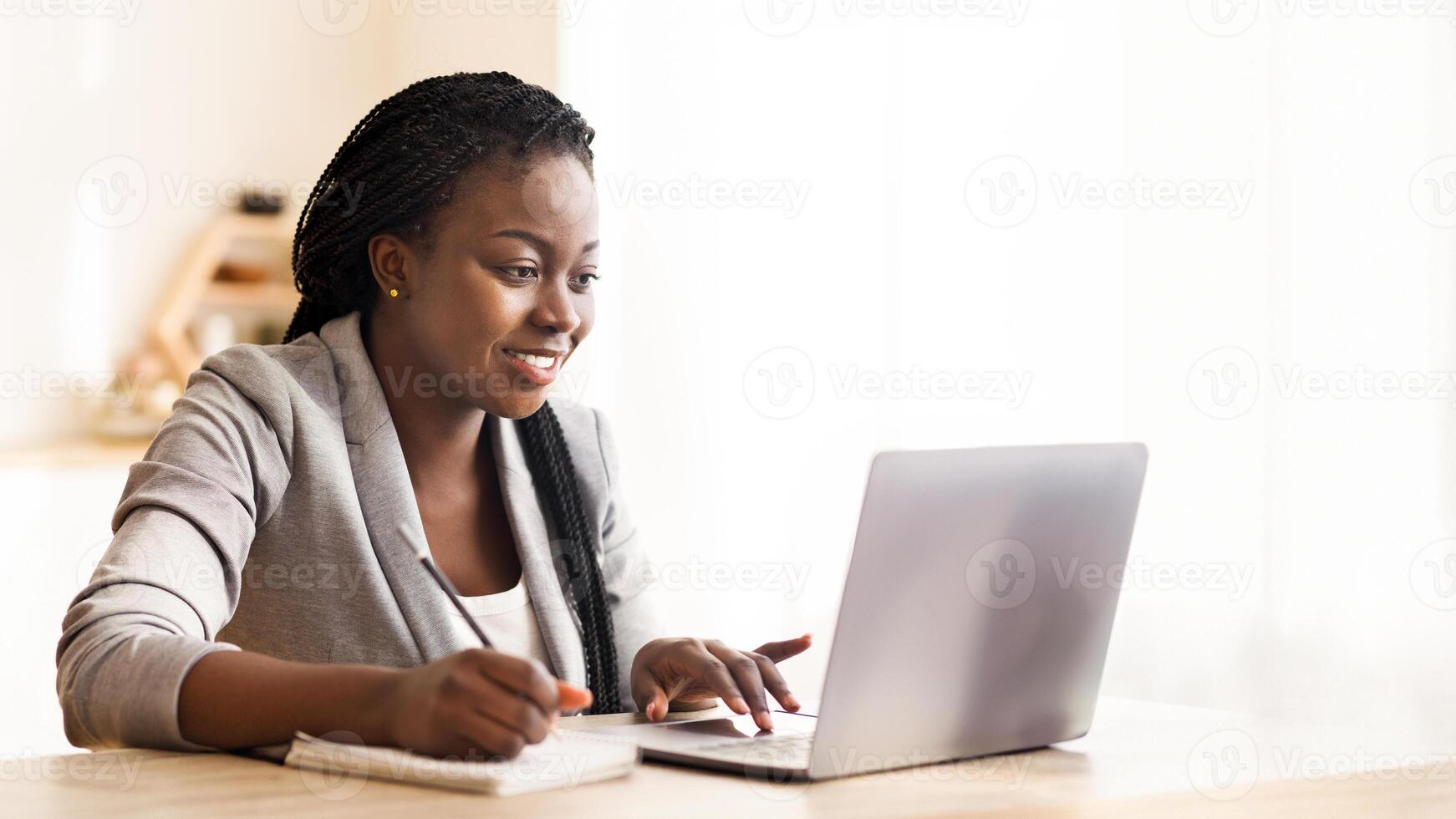 Smiling Black Businesswoman Working On Laptop And Taking Notes In Modern Office. Free Space For Your Text photo