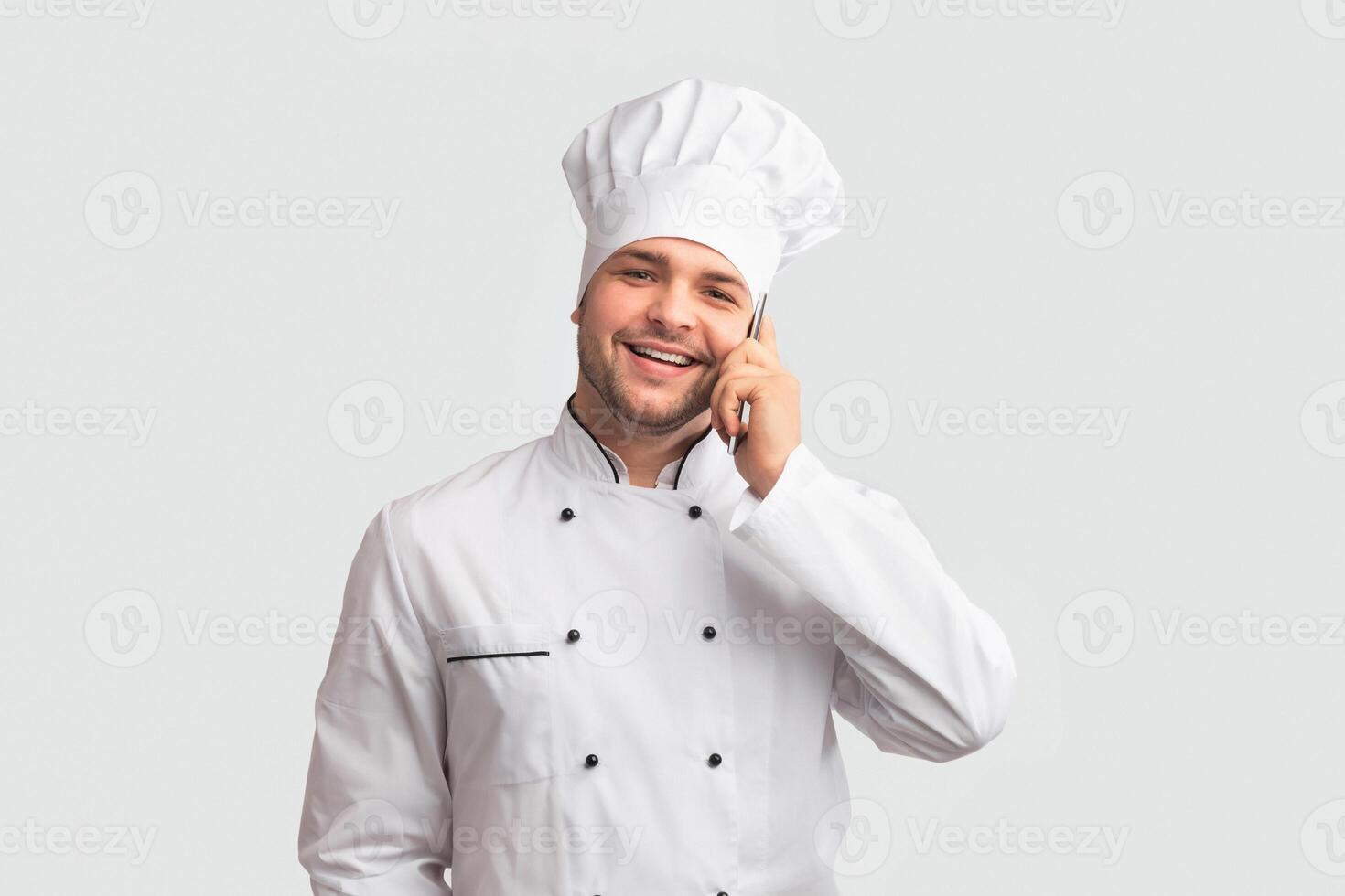 Culinary Services. Smiling Chef Cook Man In Uniform Talking On Phone Holding Clock Standing On White Studio Background. Panorama photo