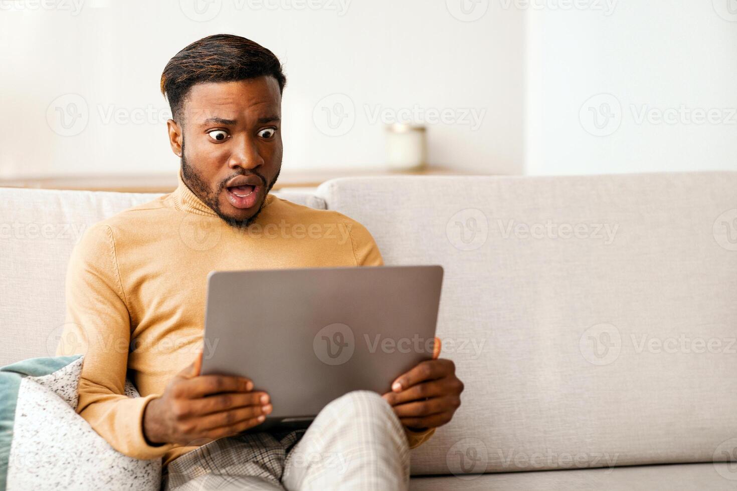 Shocked Black Guy Looking At Laptop Computer Working Sitting On Couch At Home. Selective Focus photo