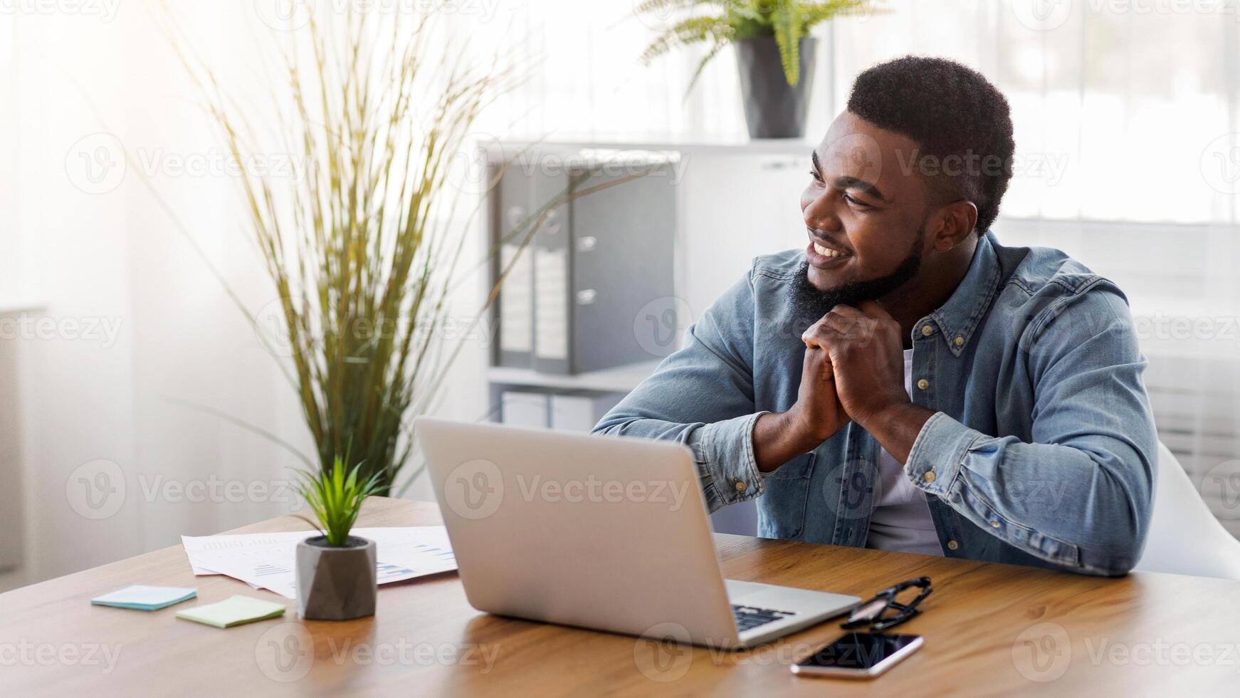 Pensive black entrepreneur dreaming about something while working in modern office, copy space photo
