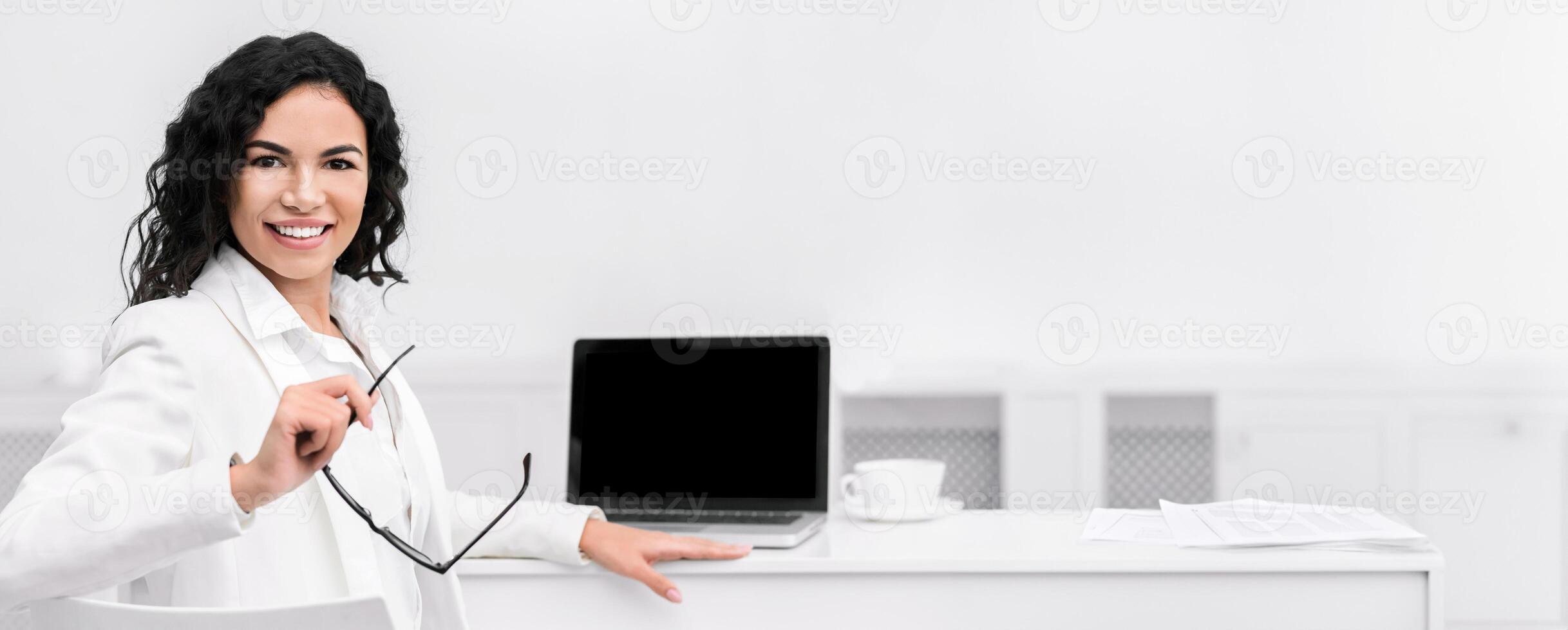 Online Education. Happy mexican teacher looking at camera using laptop with blank screen, mock up, free space photo