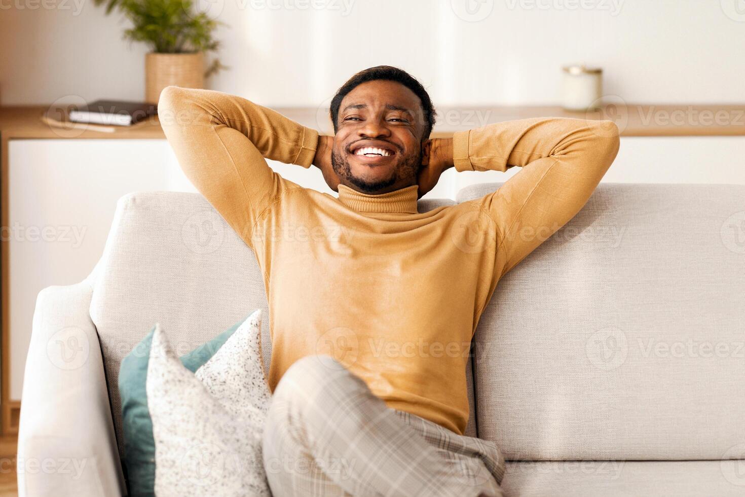 Relaxed African American Man Resting Sitting On Couch Holding Hands Behind Head At Home. Enjoying Weekend. Free Space photo