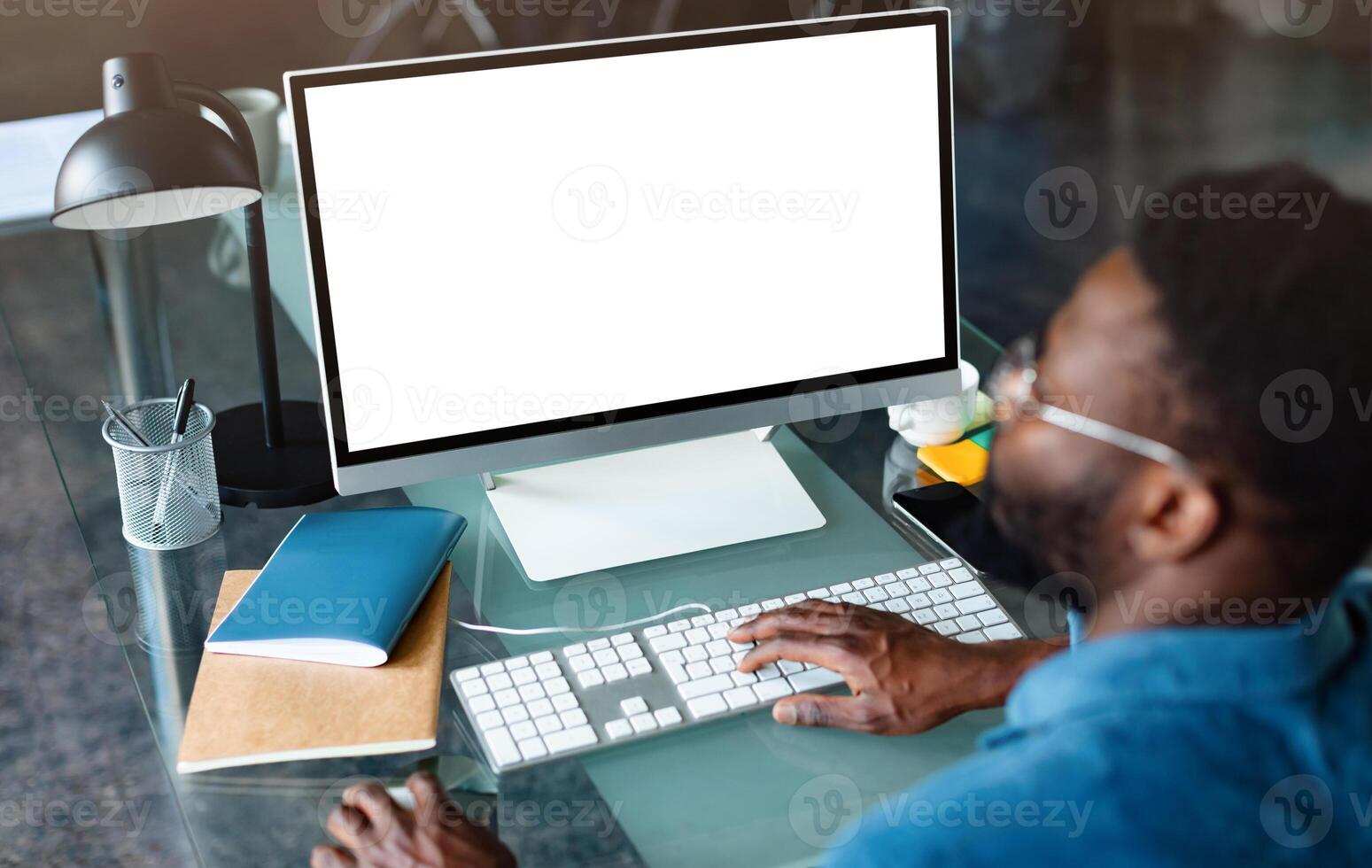 Unrecognizable black businessman using computer with empty blank screen, sitting at workplace in office, offering space for mockup on monitor. Male CEO showing place for online ad photo