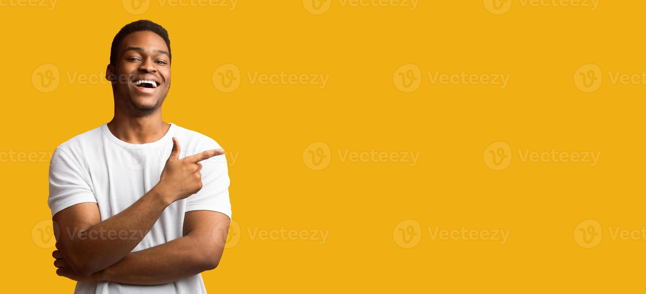 Advertisement Concept. Happy black guy pointing at copy space isolated over yellow studio background, panorama photo