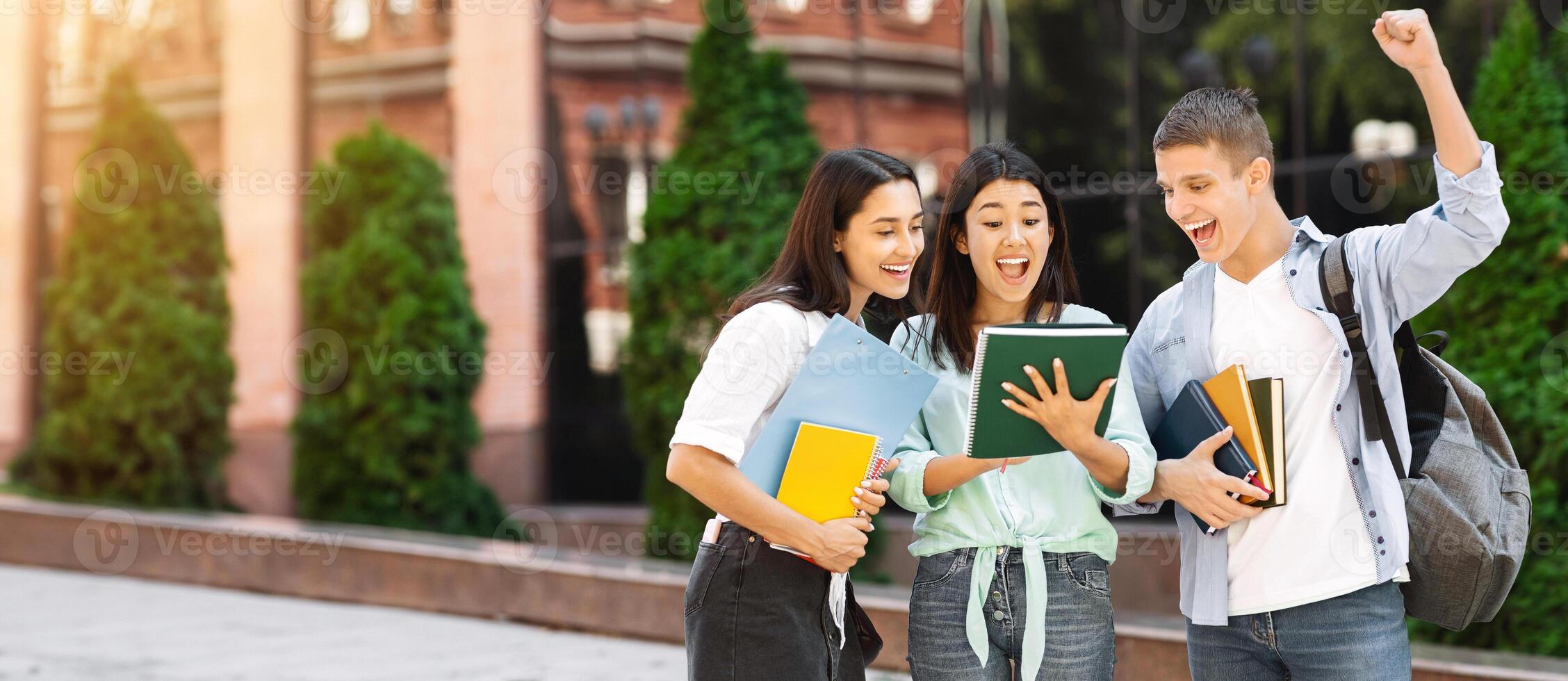Pass exams. Joyful university students reading test results standing in college campus, celebrating success photo