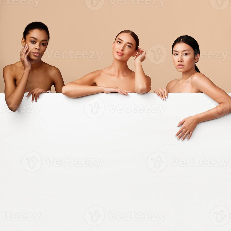 Three Diverse Women Models Posing Behind White Board For Text On Gray Studio Background. Beauty Banner With Copy Space photo