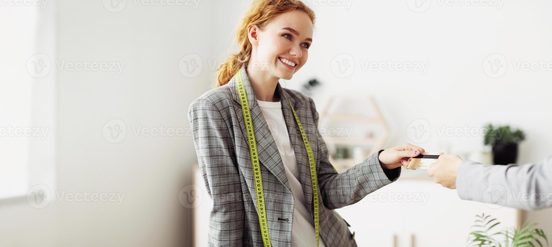 A woman wearing a blazer and a measuring tape smiles as she receives a business card from a client. photo