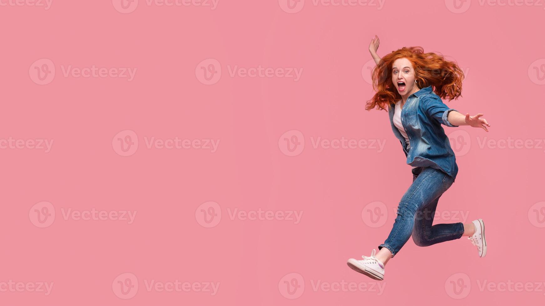Activity and happiness. Excited redhead woman having fun, jumping on pink studio background photo