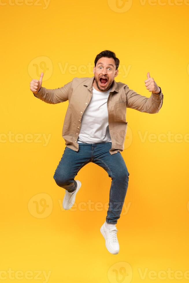 A man is captured mid-jump, with his hands raised above his head in the air. He appears to be in a moment of excitement or celebration, leaping energetically. photo