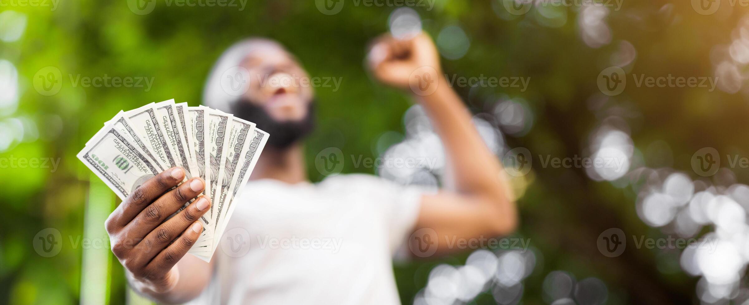 Loterry win. Happy african american man holding fan of dollars in hand outdoor, panorama photo
