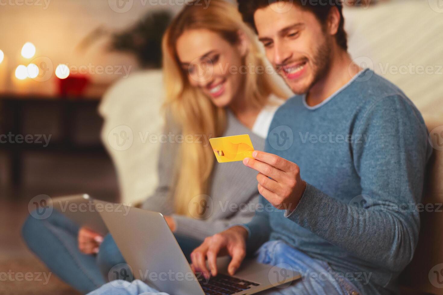 Husband And Wife Shopping Online Using Laptop And Credit Card Sitting On Sofa Indoor. E-Commerce Concept. Selective Focus photo