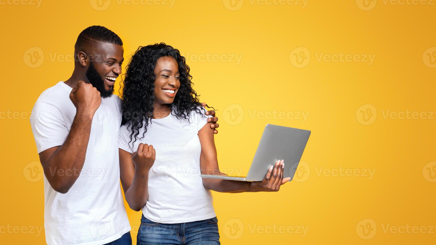 Cheerful African American Millennial Guy and Girl Celebrating Win Laptop, smiling on yellow background, copy space photo