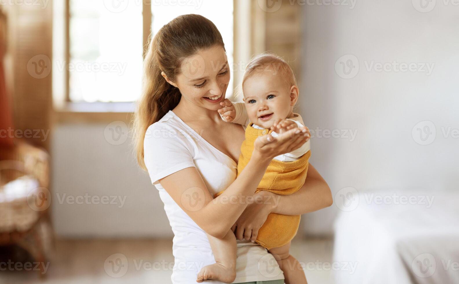 Happy maternity leave time, motherhood concept. Beautiful young mother enjoying pastime with her lovely baby, mom holding adorable little child in her arms and smiling, free space photo